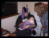 Mr. Graves giving Logan a bottle, Ms. McKennon leaning in.