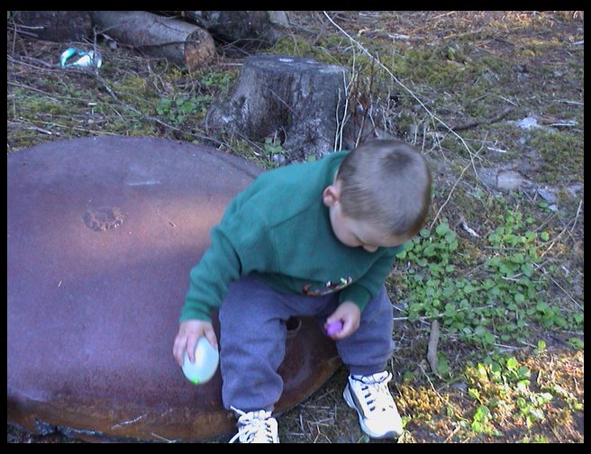 Logan sitting on the unused half of our firepit w/ waterballoons in hand.